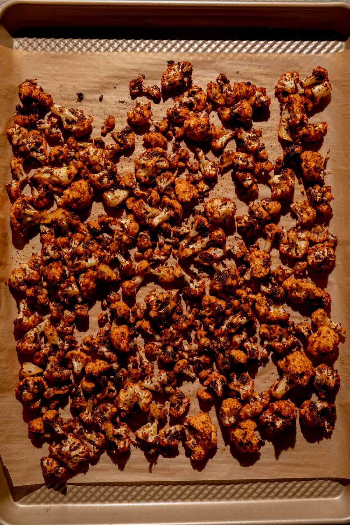 Roasted cauliflower on a parchment  lined baking sheet. 