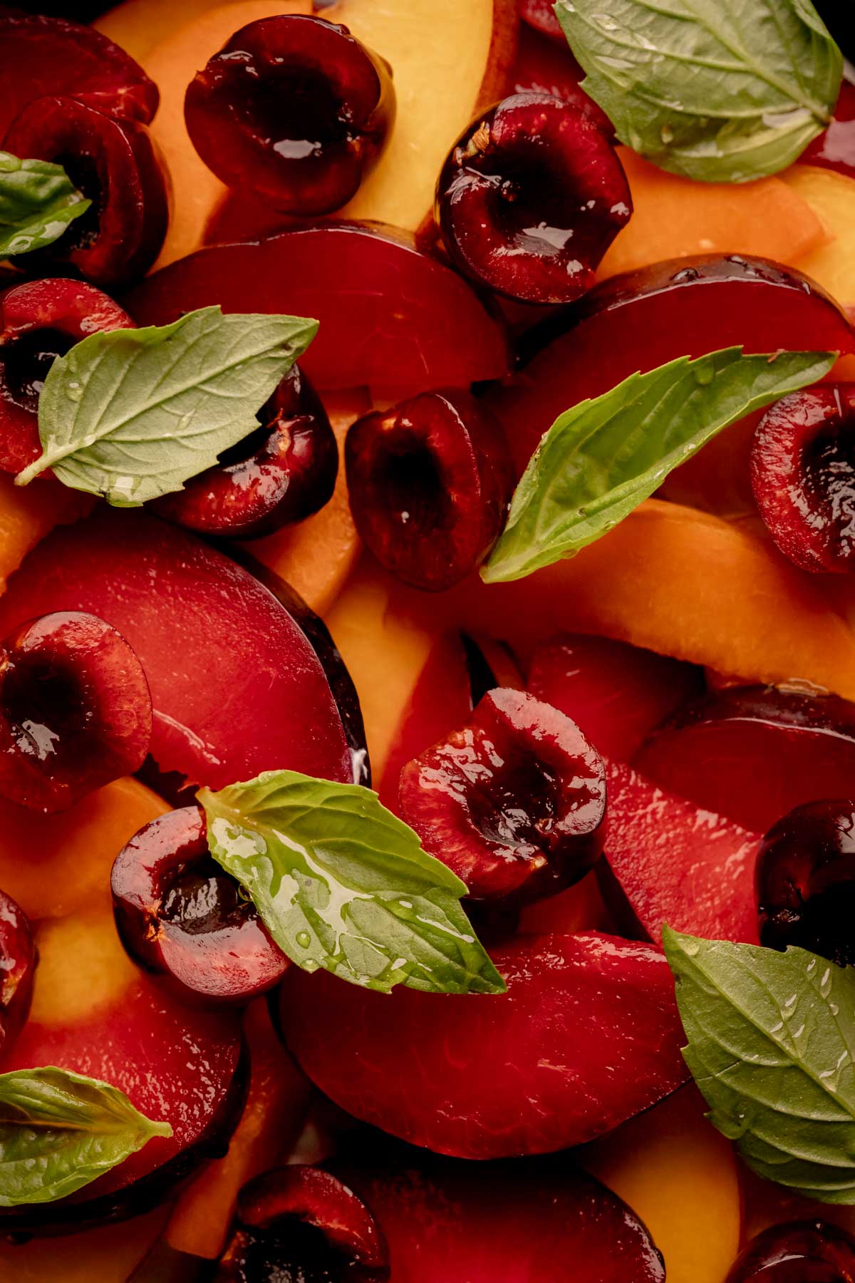 Sliced stone fruit with thai basil leaves and drizzle of honey on top.