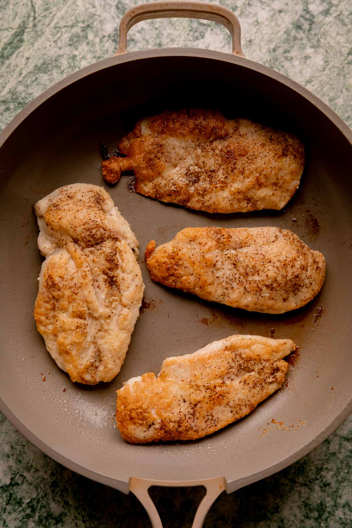 Golden brown chicken fillets in a pan.