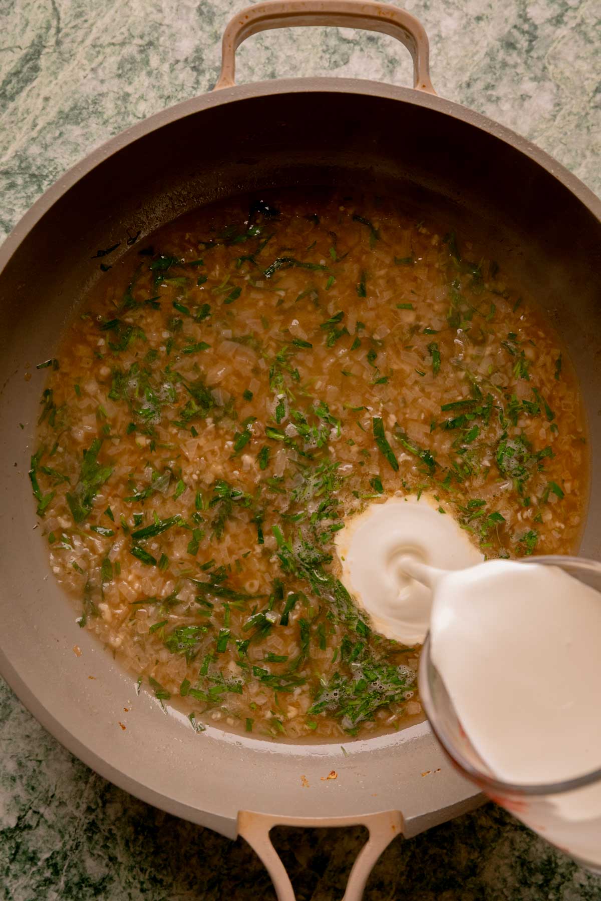 Heavy cream being poured into a pan of tarragon sauce.