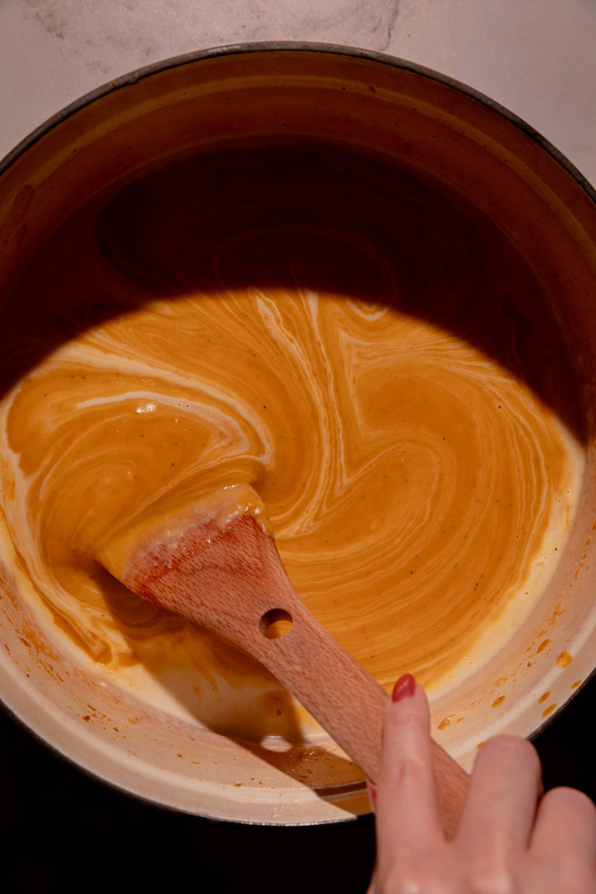 A hand stirring coconut milk into sweet potato soup.