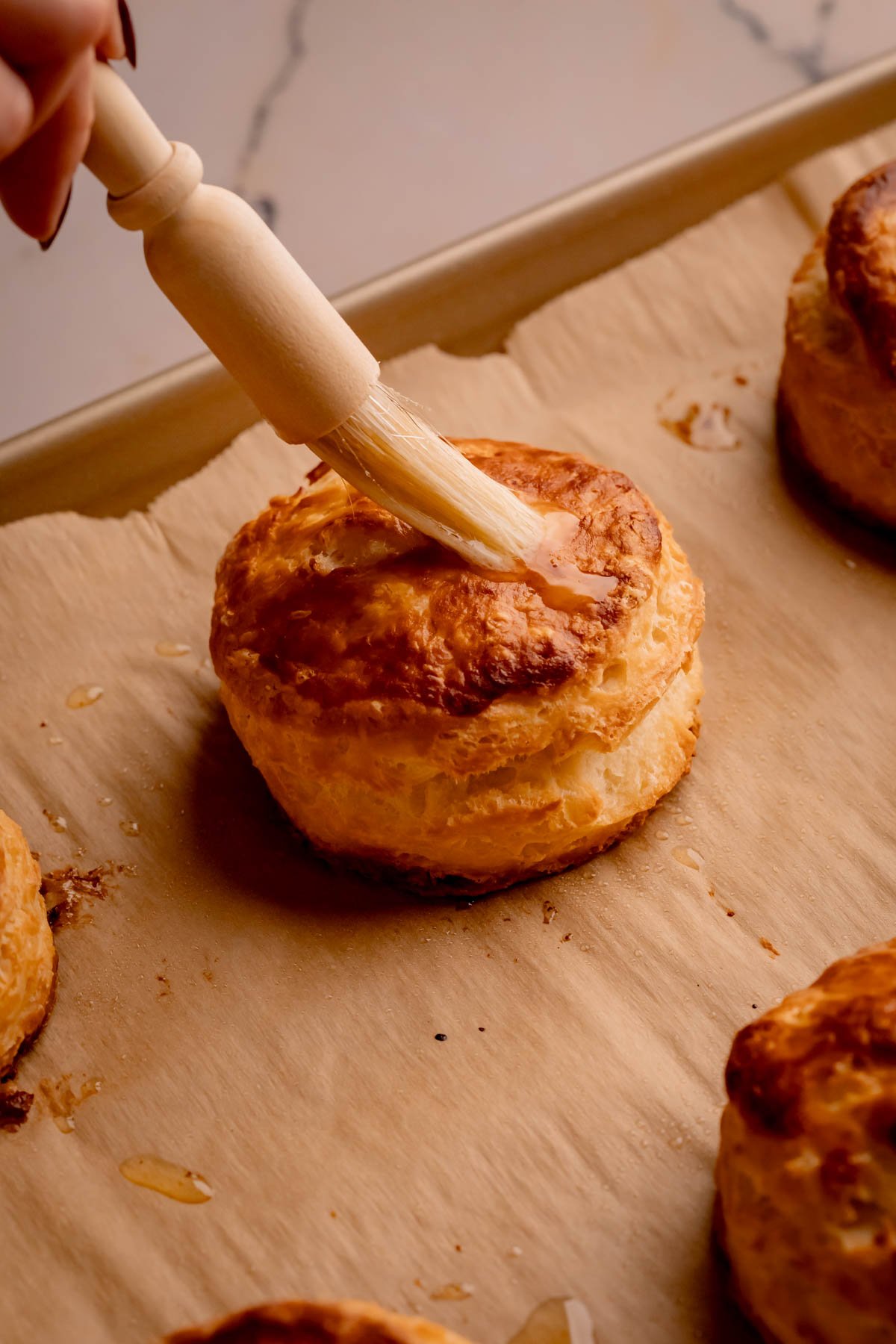 A baked buttermilk biscuit with butter being brushed on top.