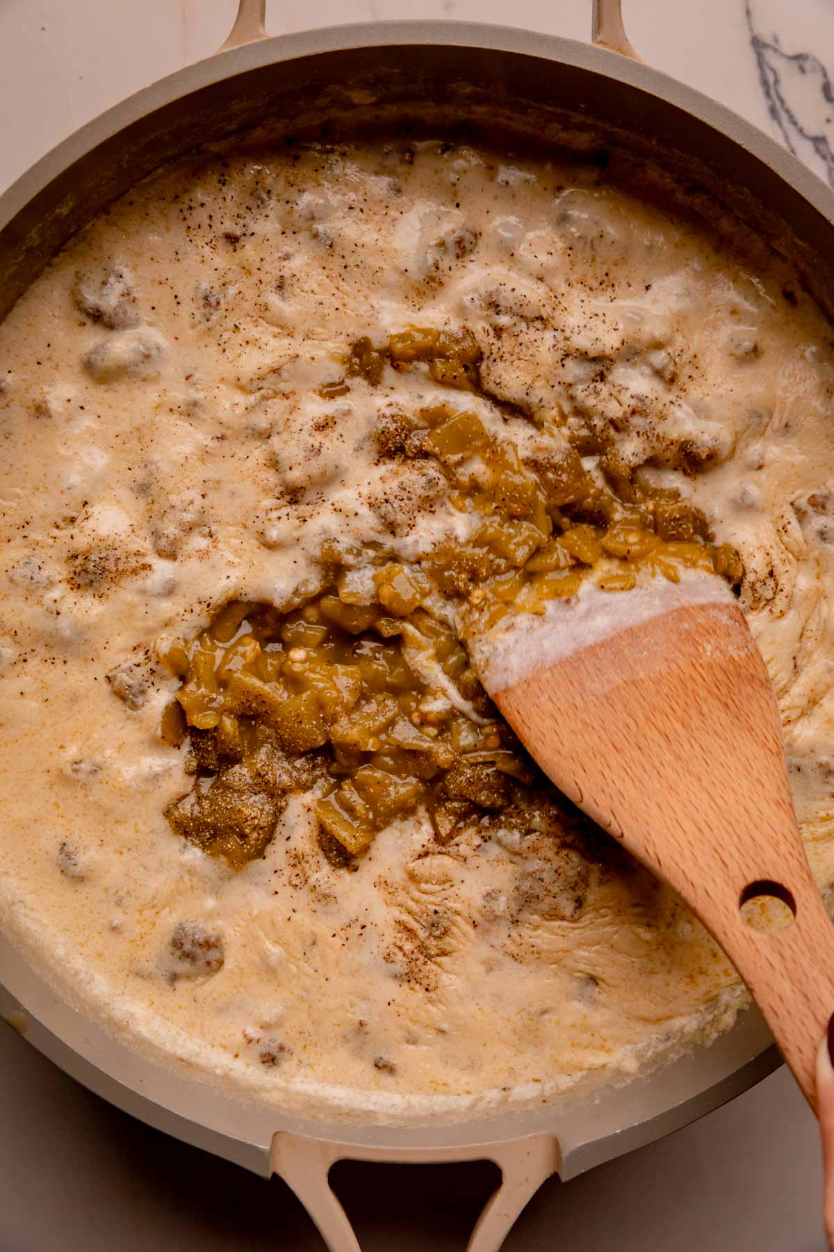 Sausage gravy with diced green chiles being mixed in.