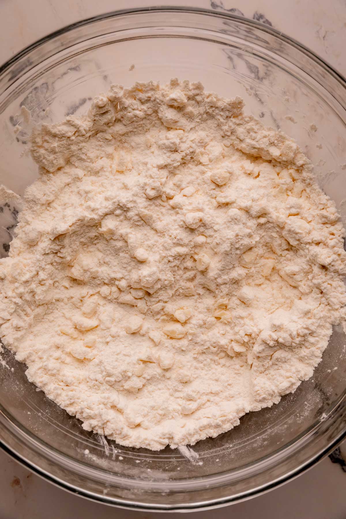 A bowl of dry ingredients with pea sized blobs of butter mixed in.