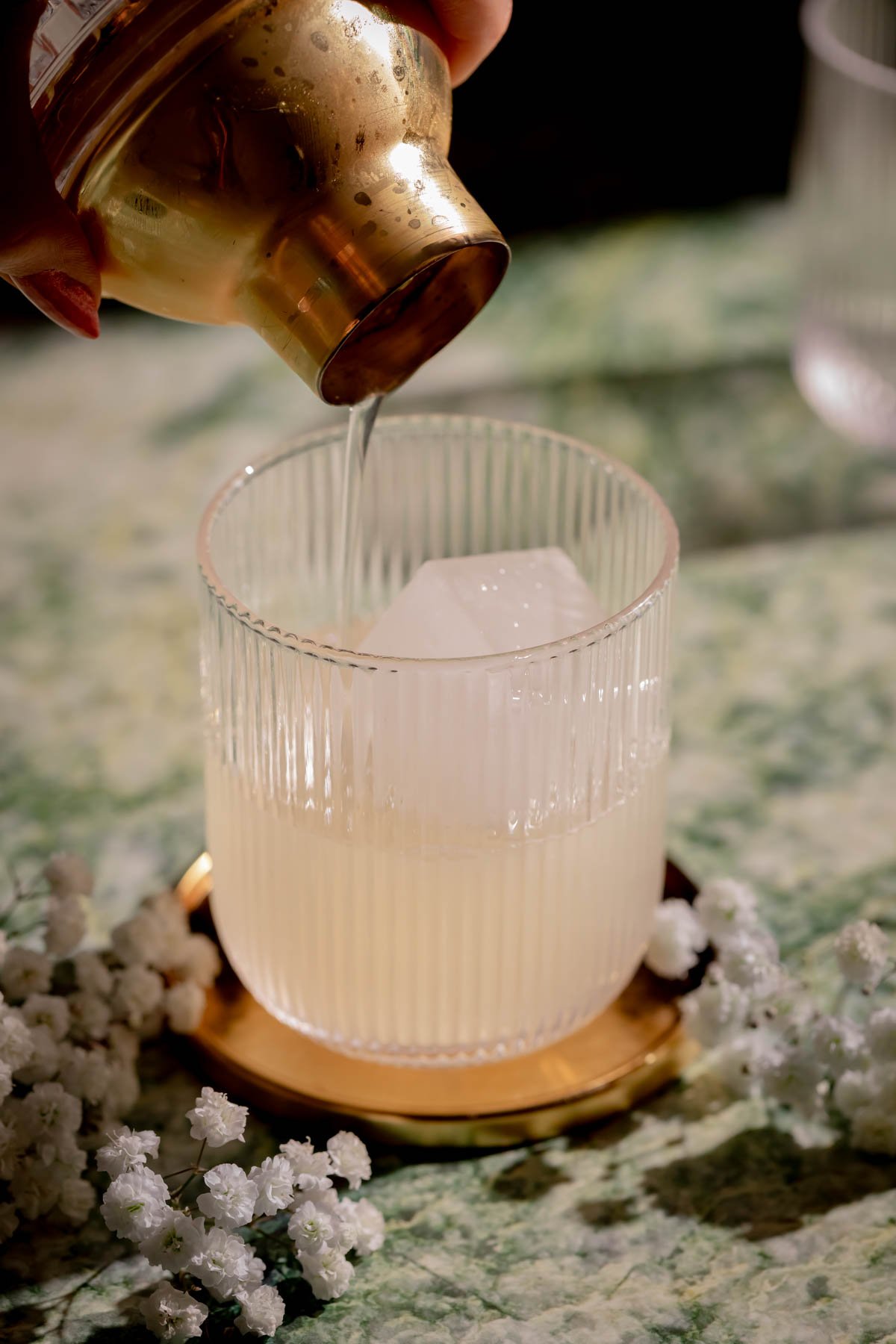 A hand pouring a drink into a glass from a cocktail shaker.