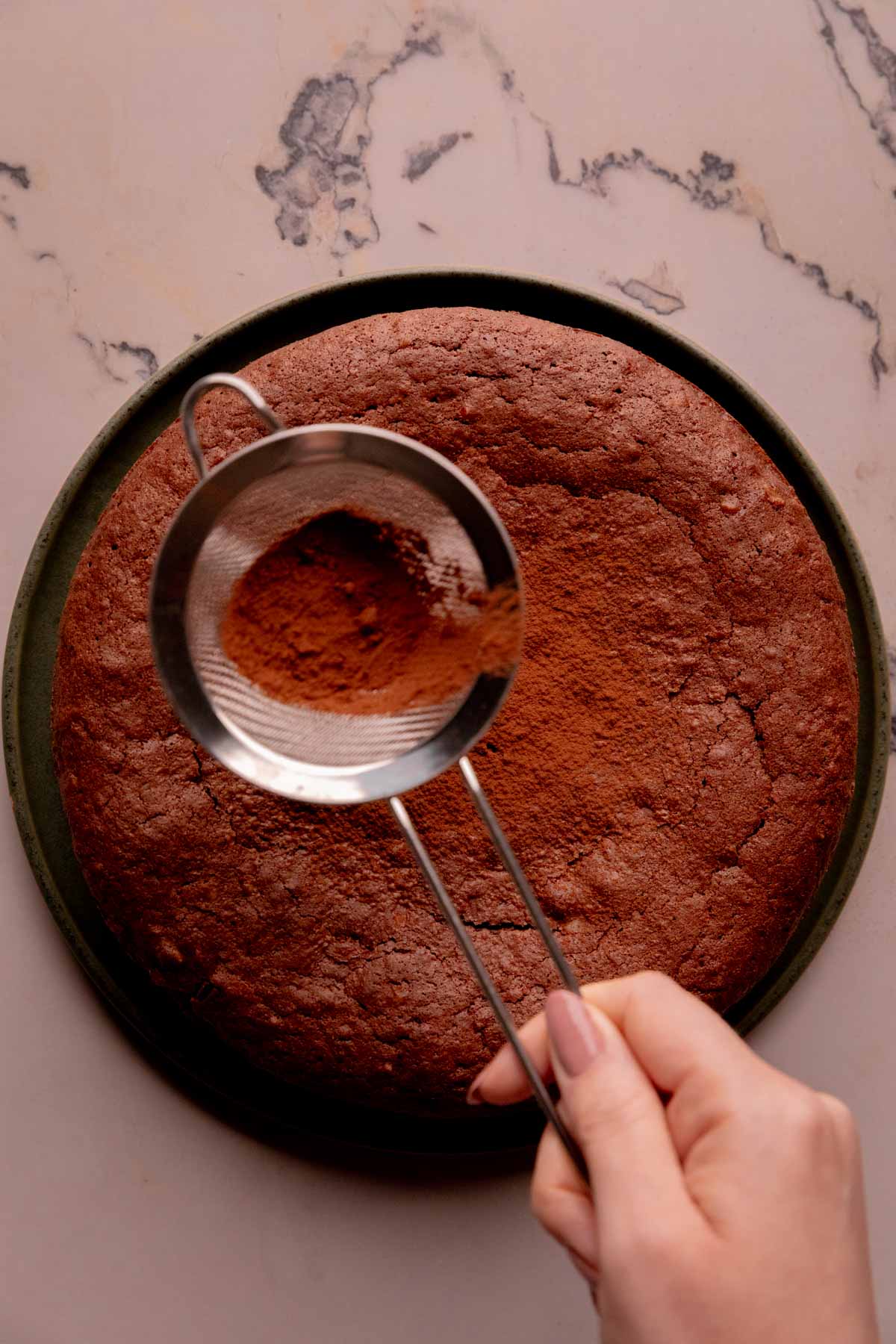 A hand sifting cocoa powder onto a torta caprese.