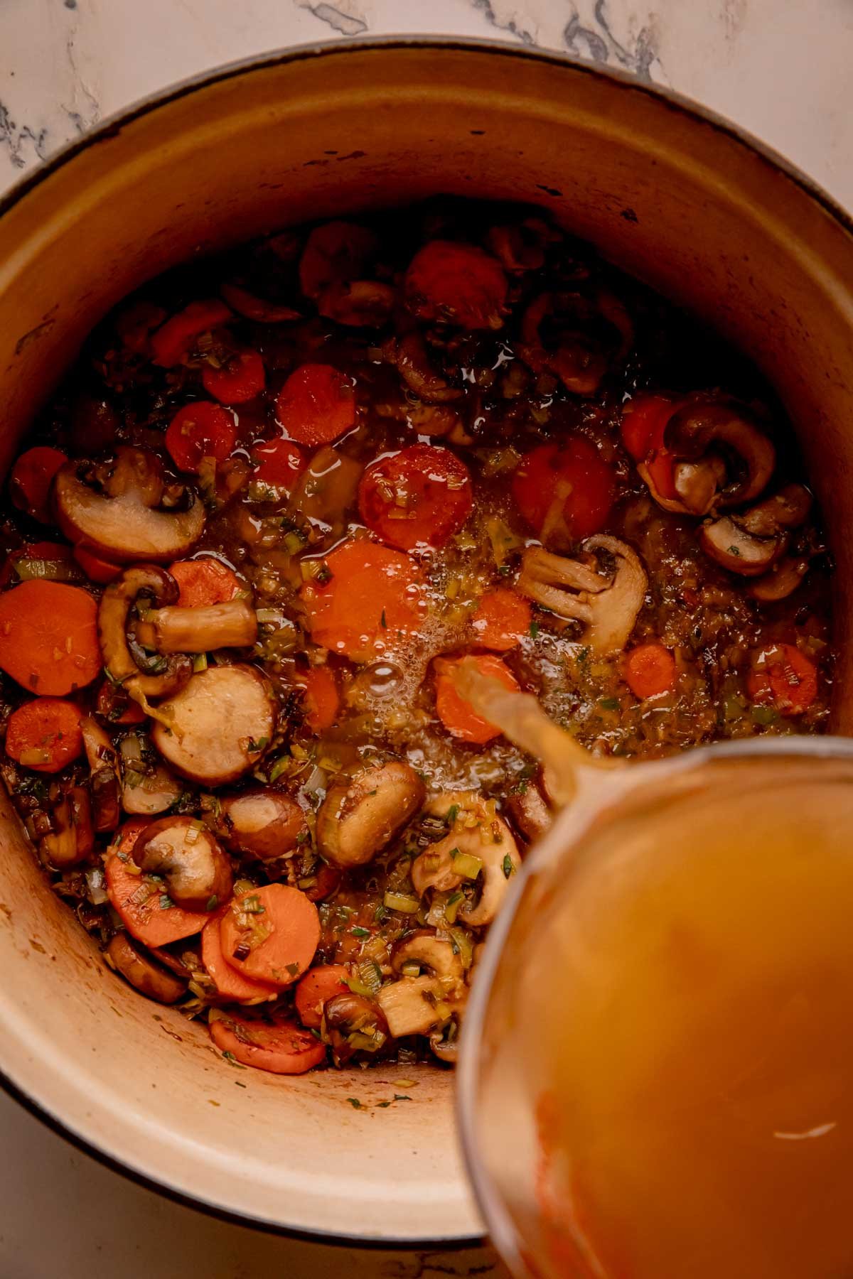 Chicken stock being poured into a dutch oven with sautéed vegetables.