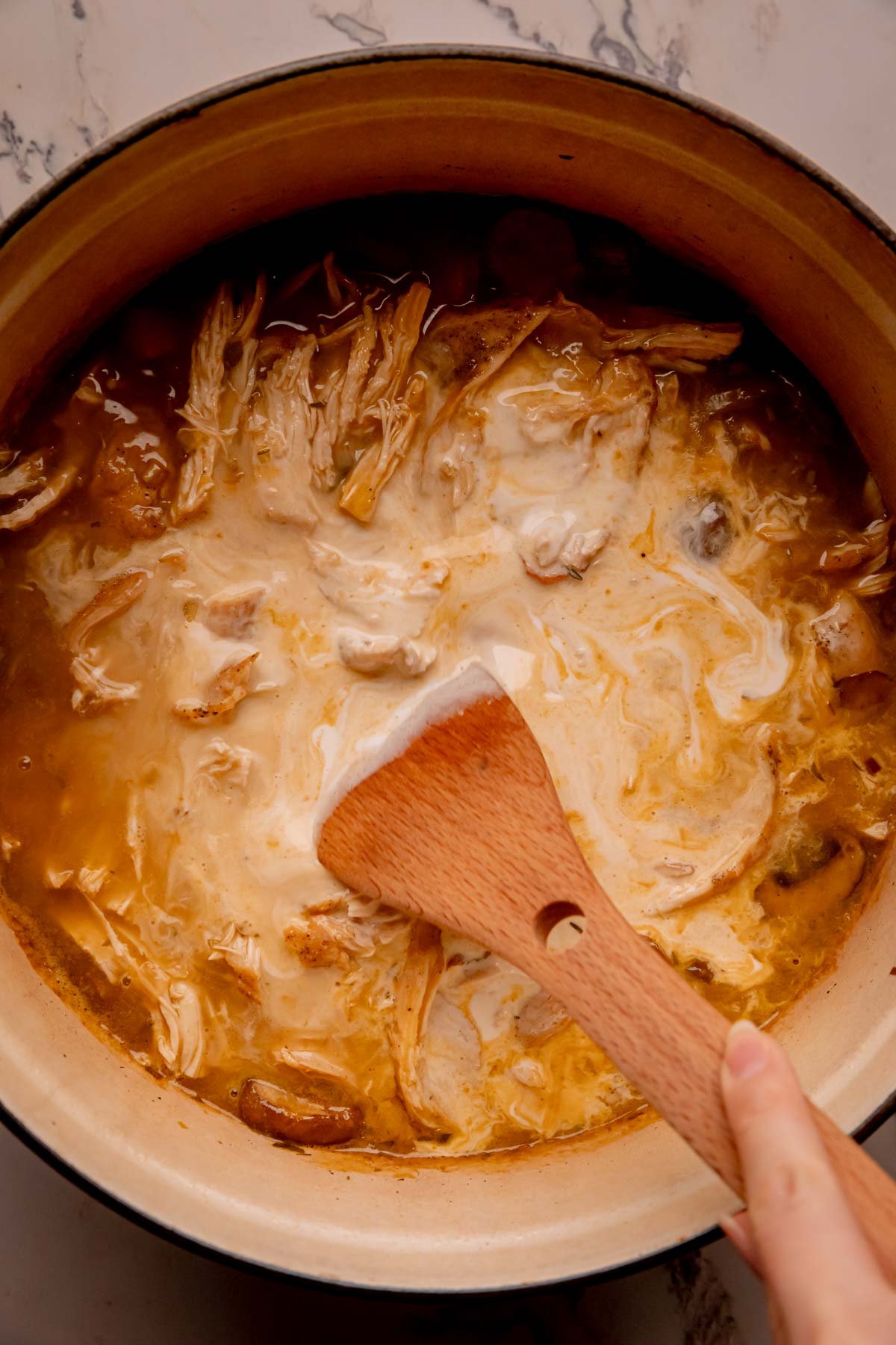 A hand stirring heavy cream into chicken soup.