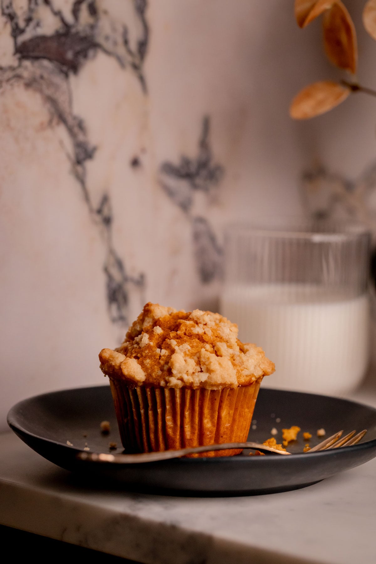 A five spice pumpkin muffin on a plate with a fork and a glass of milk.