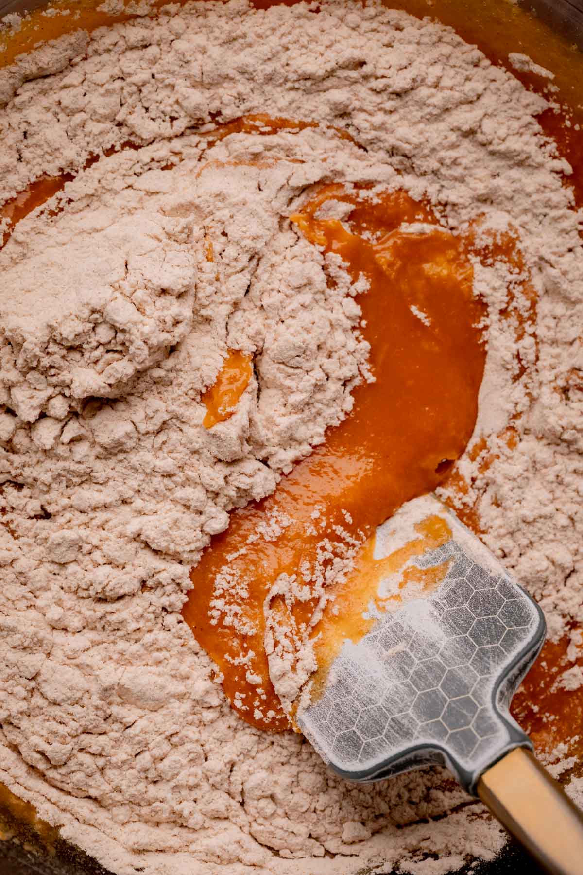 Flour being folded into pumpkin batter with a silicone spatula.