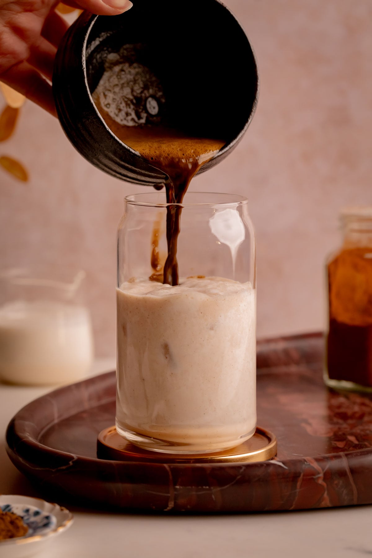 A hand pouring hojicha tea into a glass of banana milk.