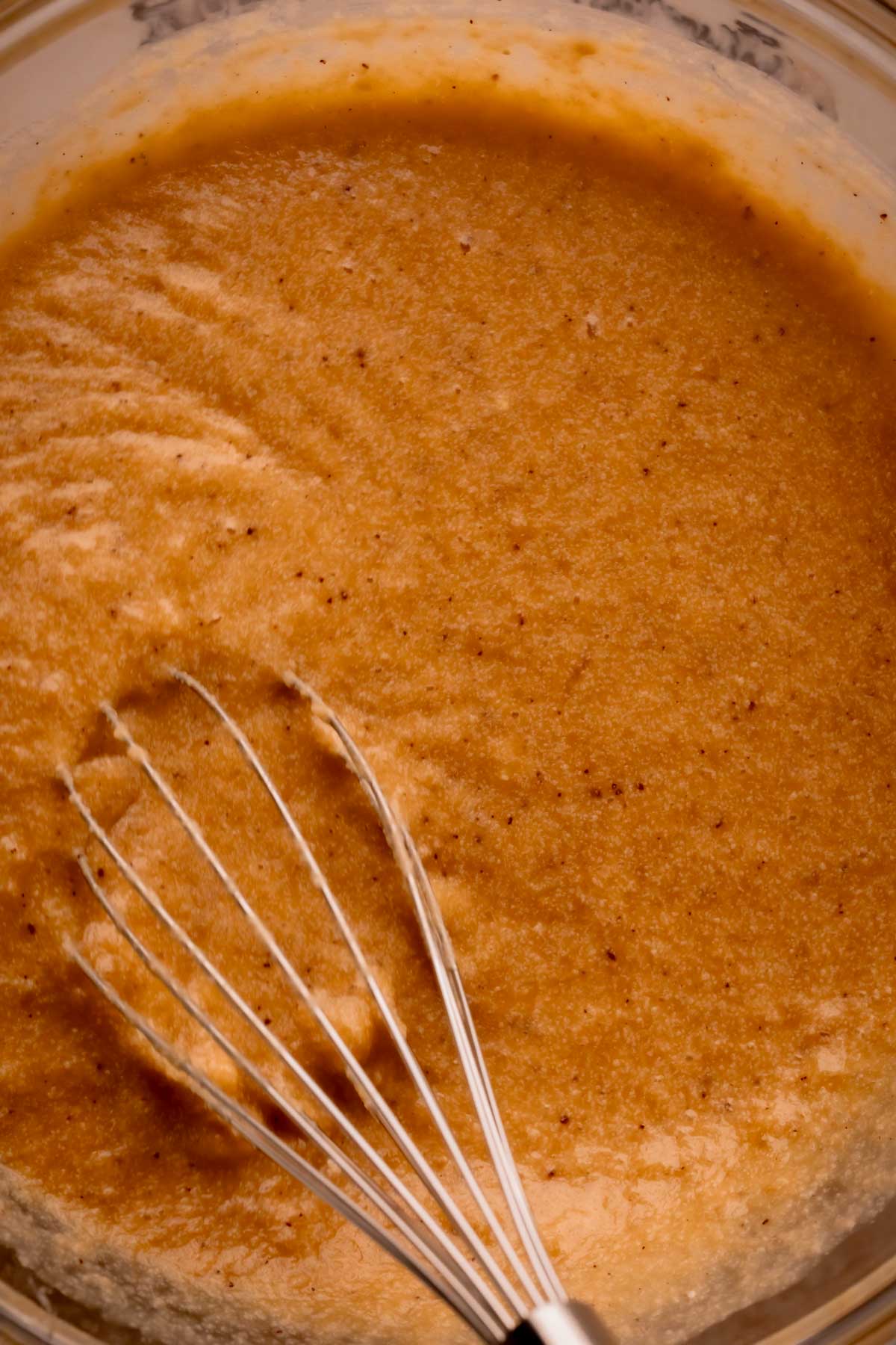A whisk mixing together wet ingredients for banana bread batter.