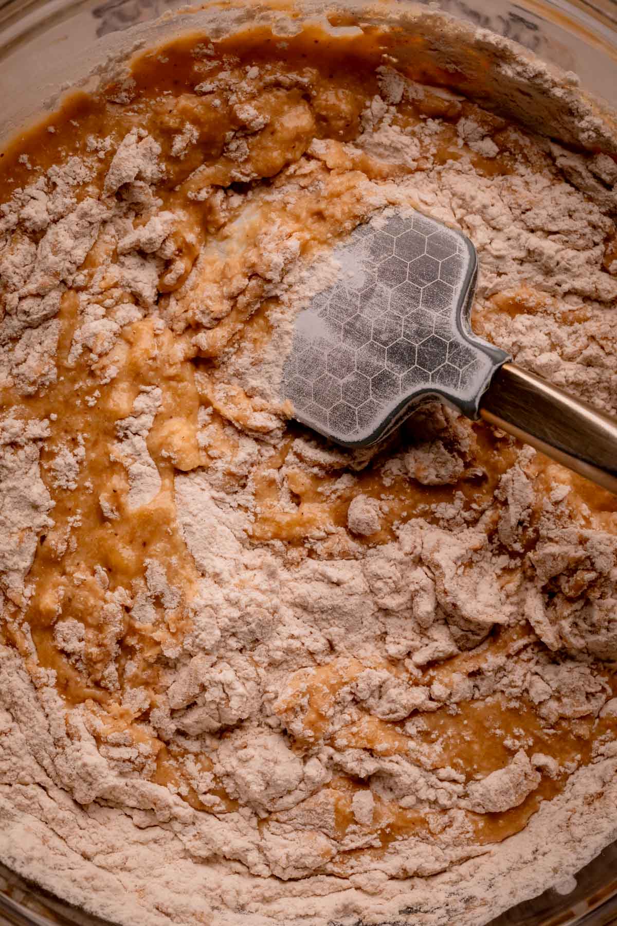 A silicone spatula folding dry ingredients into wet ingredients.