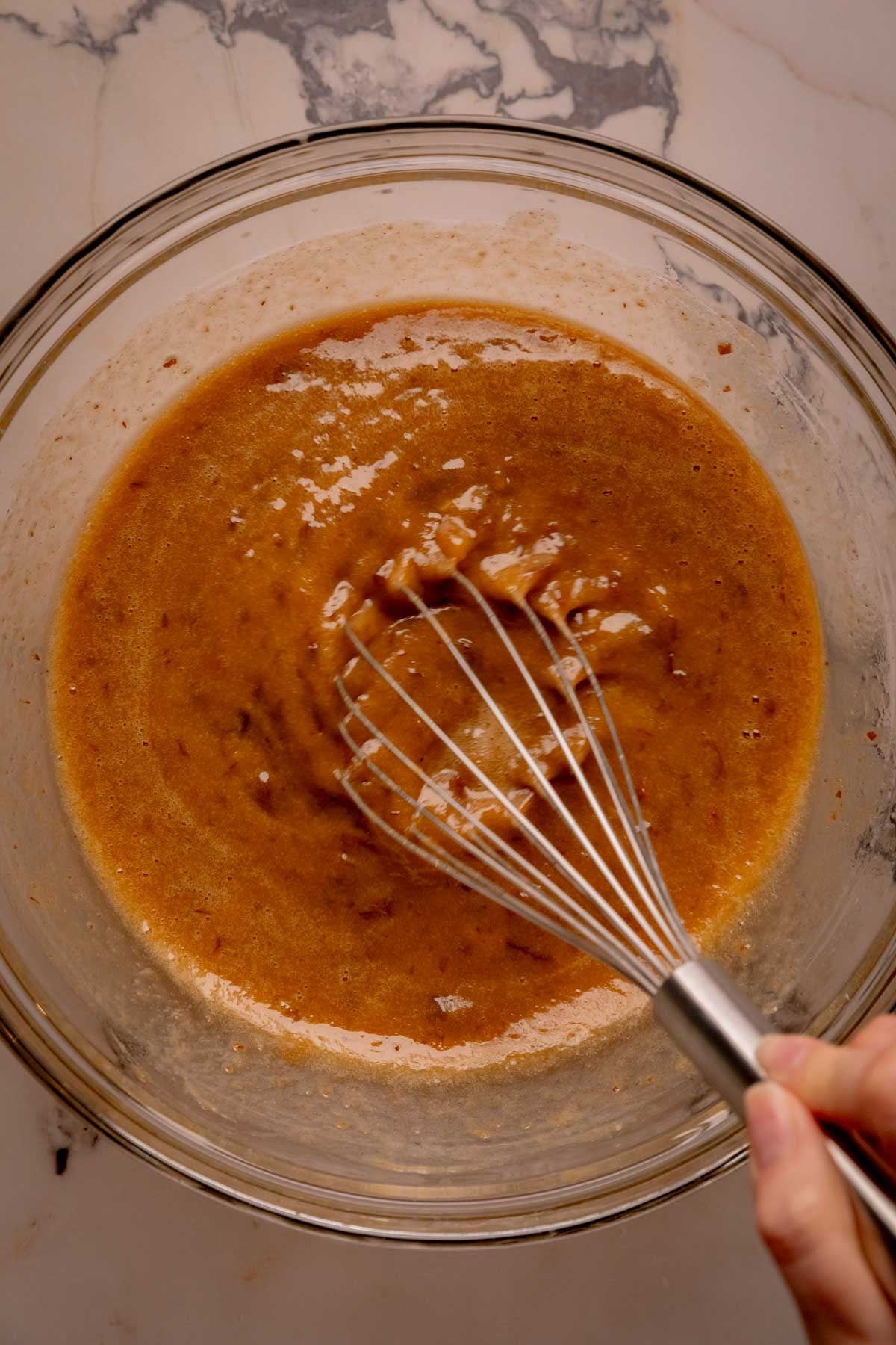 A hand whisking together wet ingredients in a bowl.