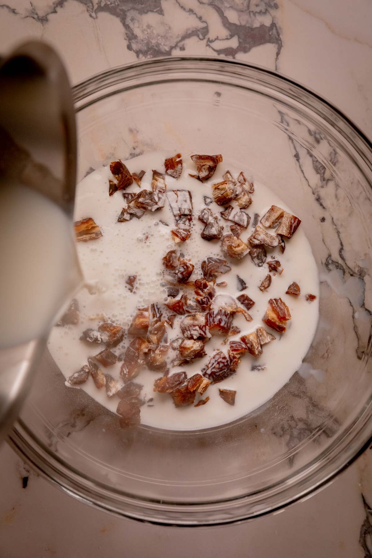 Boiling milk being poured over a bowl of chopped dates and baking soda.