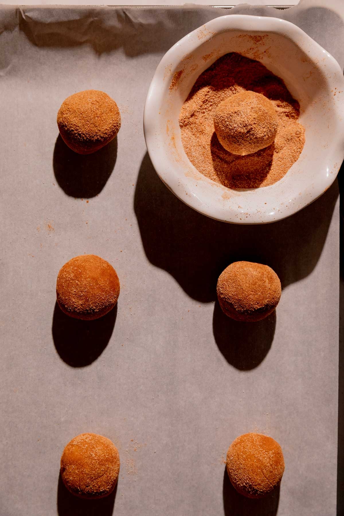 Cookie dough balls rolled in cinnamon sugar on a baking sheet.