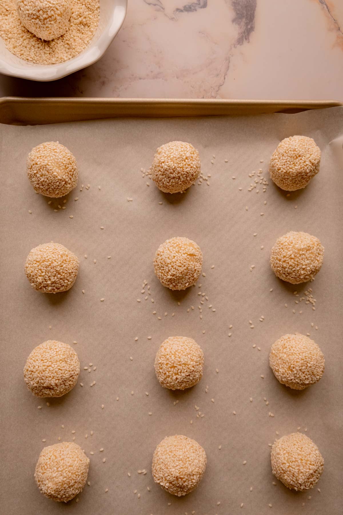 Sesame rolled cookie dough balls on a lined baking sheet.