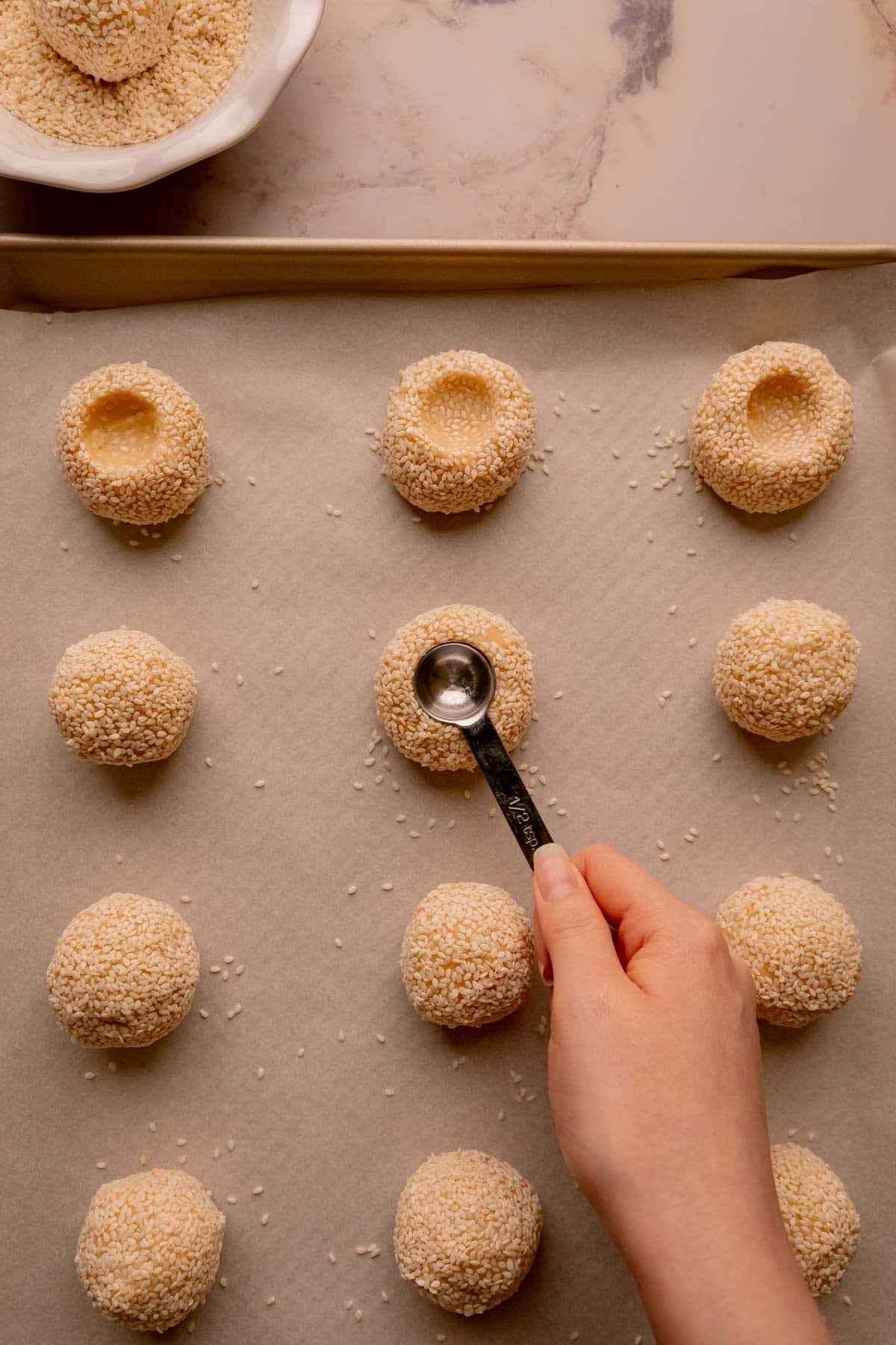 A hand using a half teaspoon to make indents in the center of cookie dough balls.