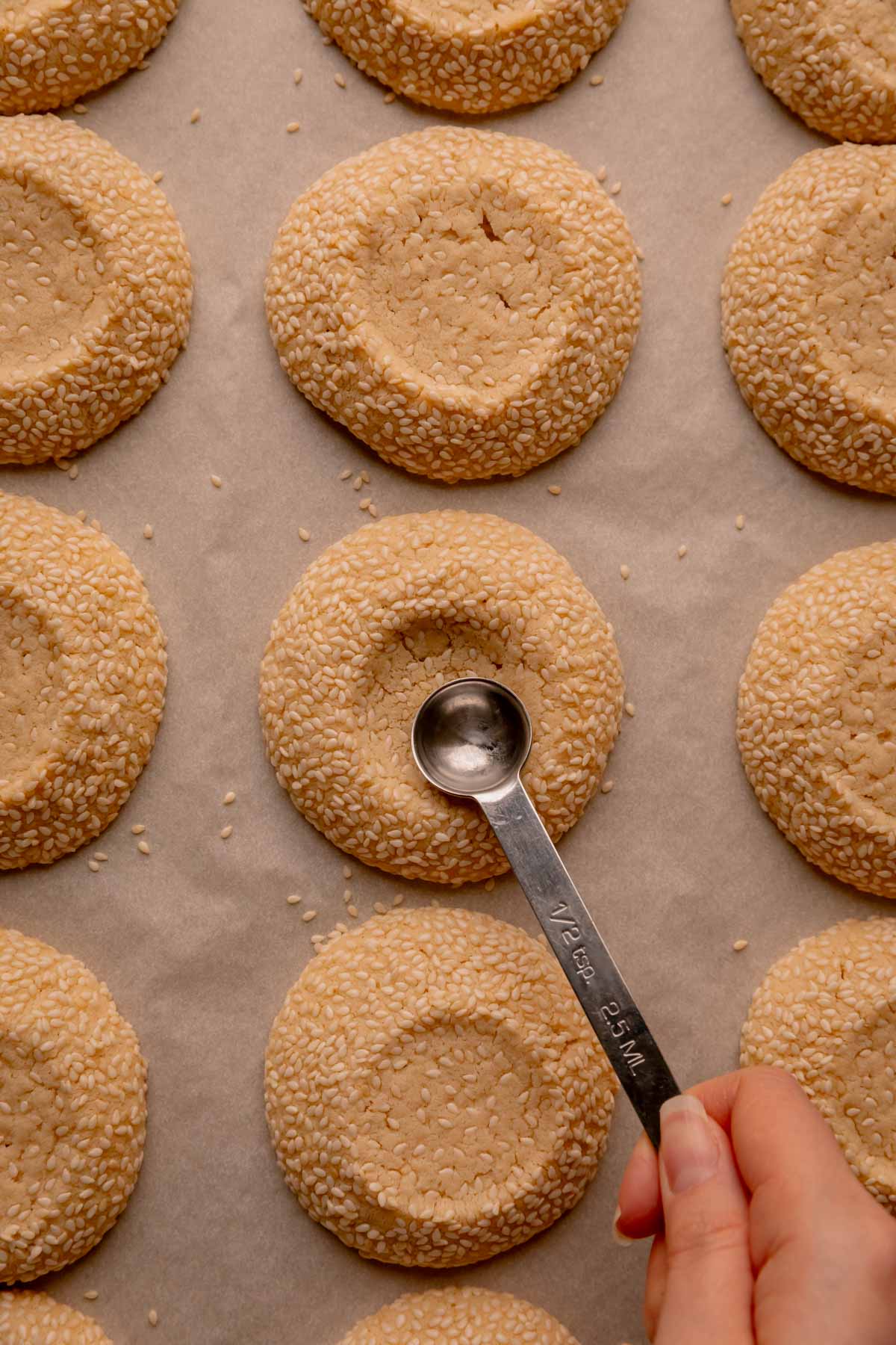 A hand reshaping the indent in a baked cookie with a half teaspoon.