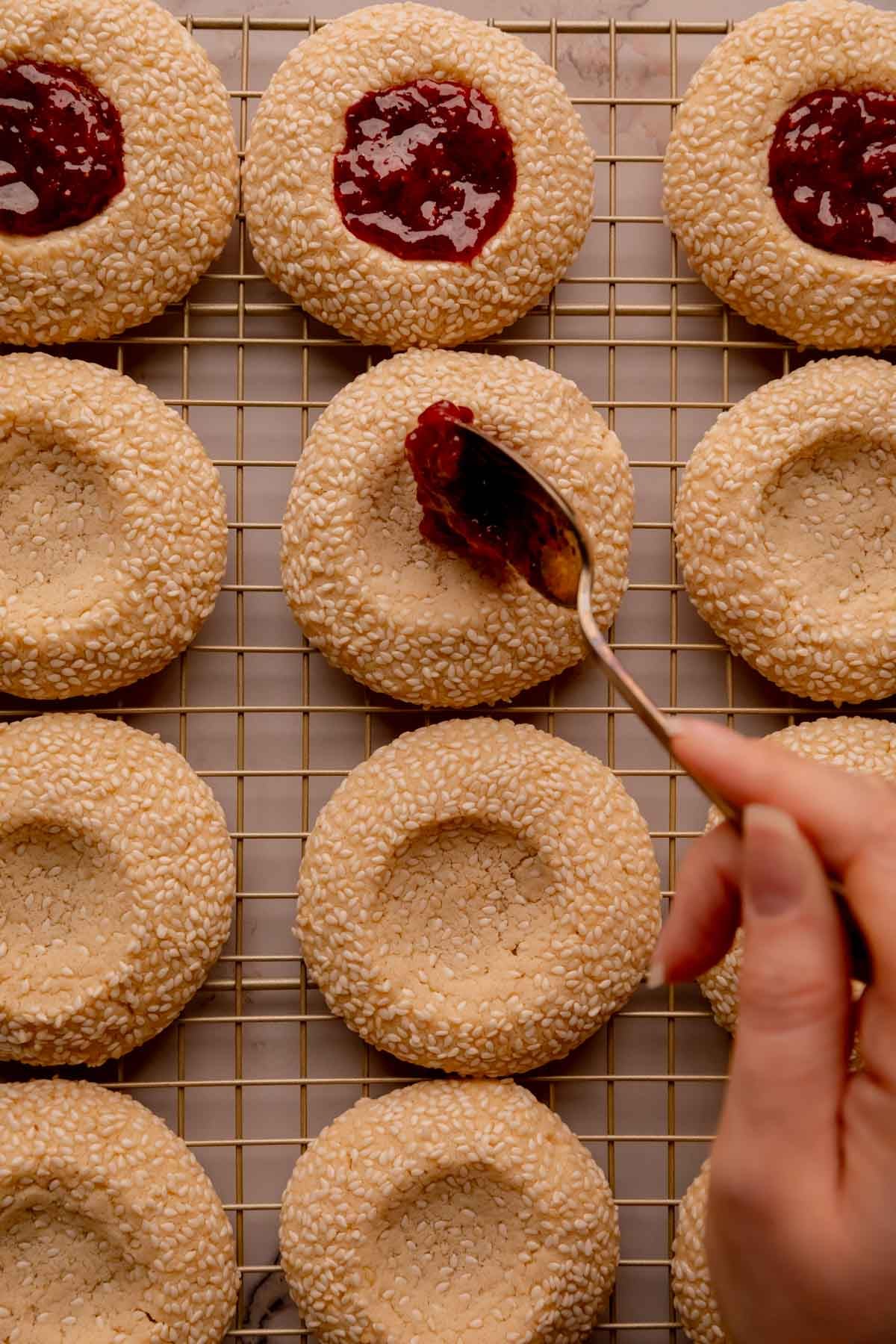 A hand spooning strawberry sumac jam into the center of a cookie.