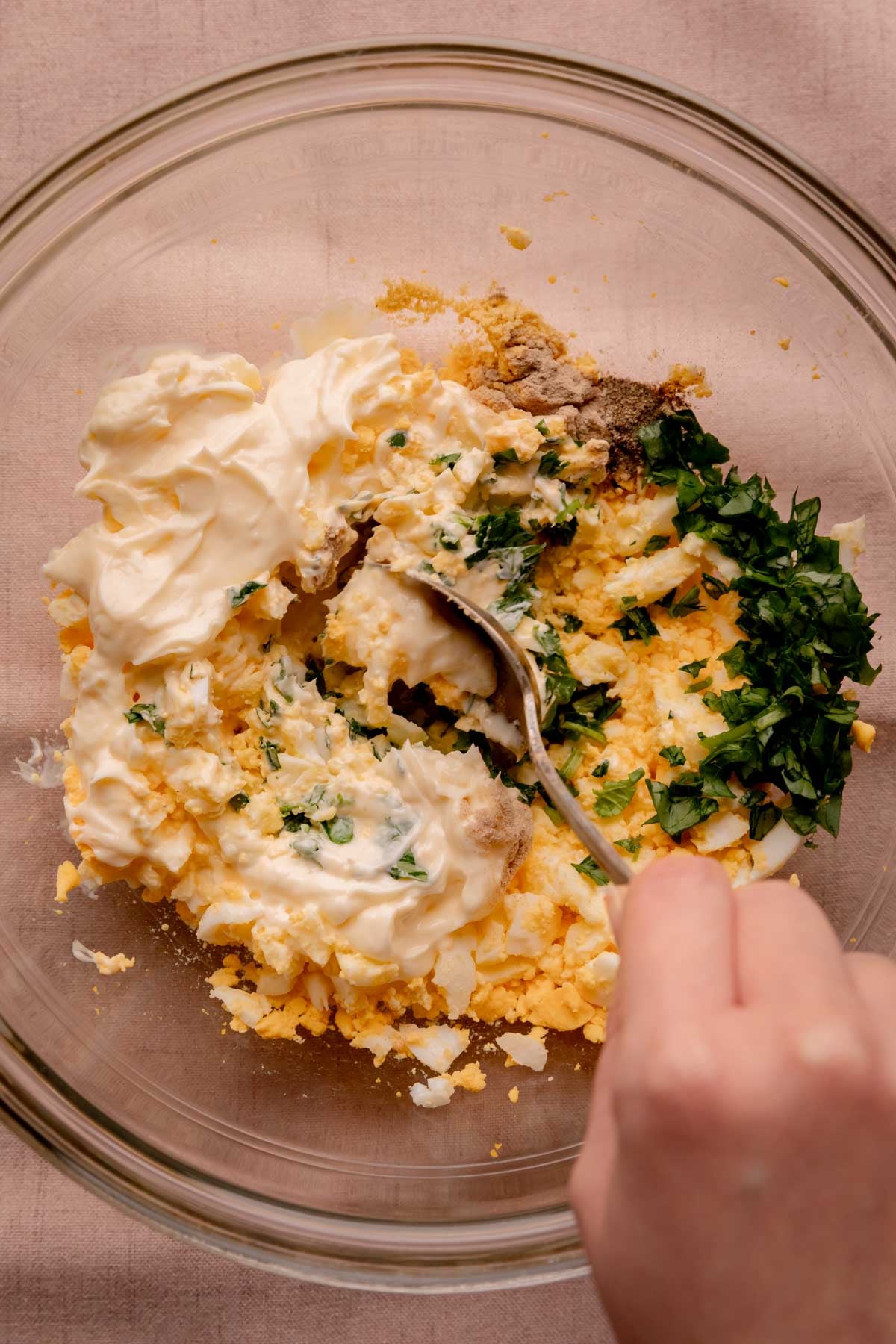 A hand mixing a bowl of egg salad.