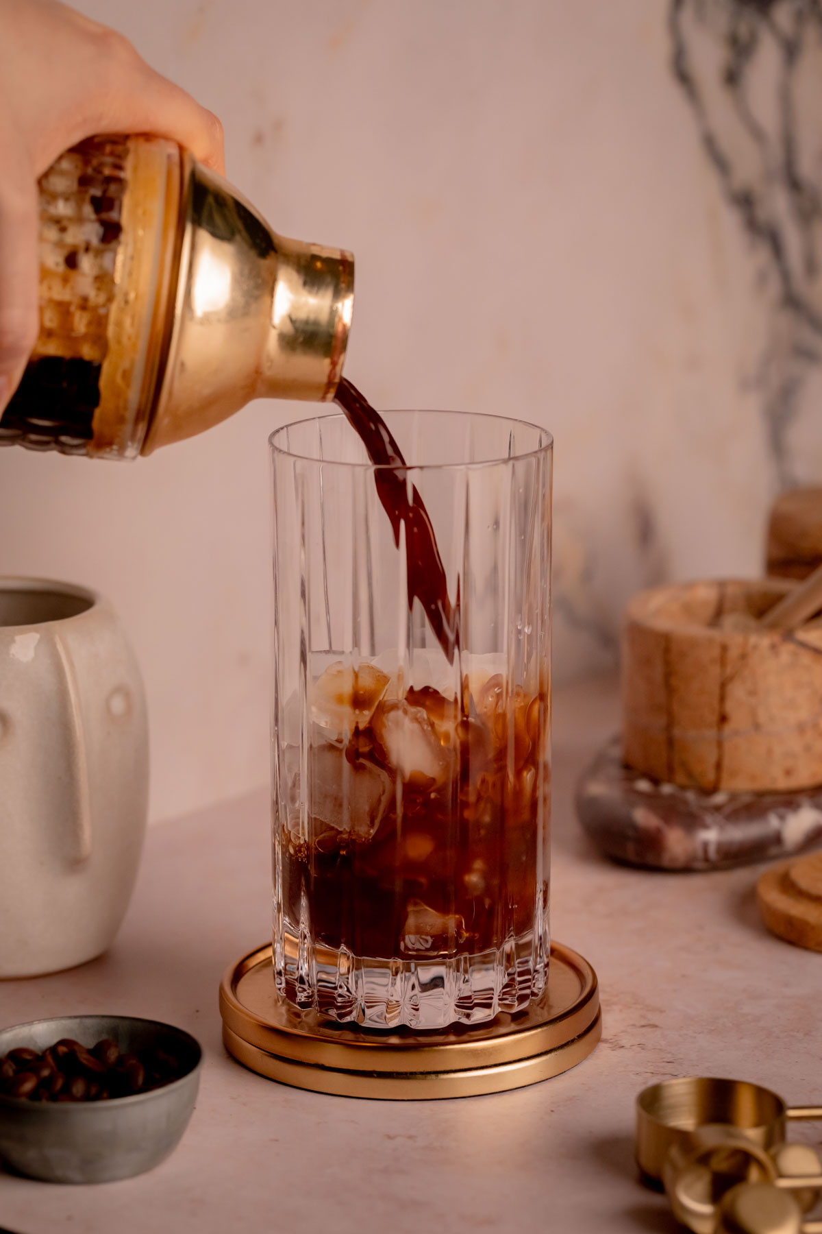A hand pouring espresso out of a cocktail shaker into a glass with ice.