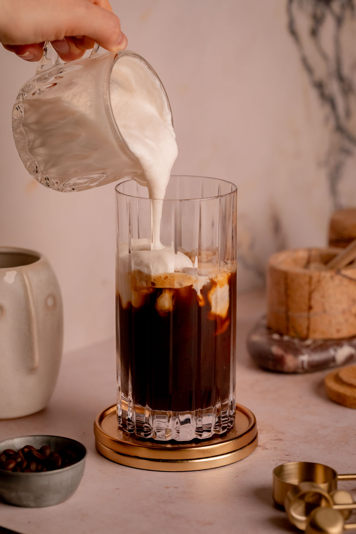 A hand pouring cold foam over a glass of iced shaken espresso.