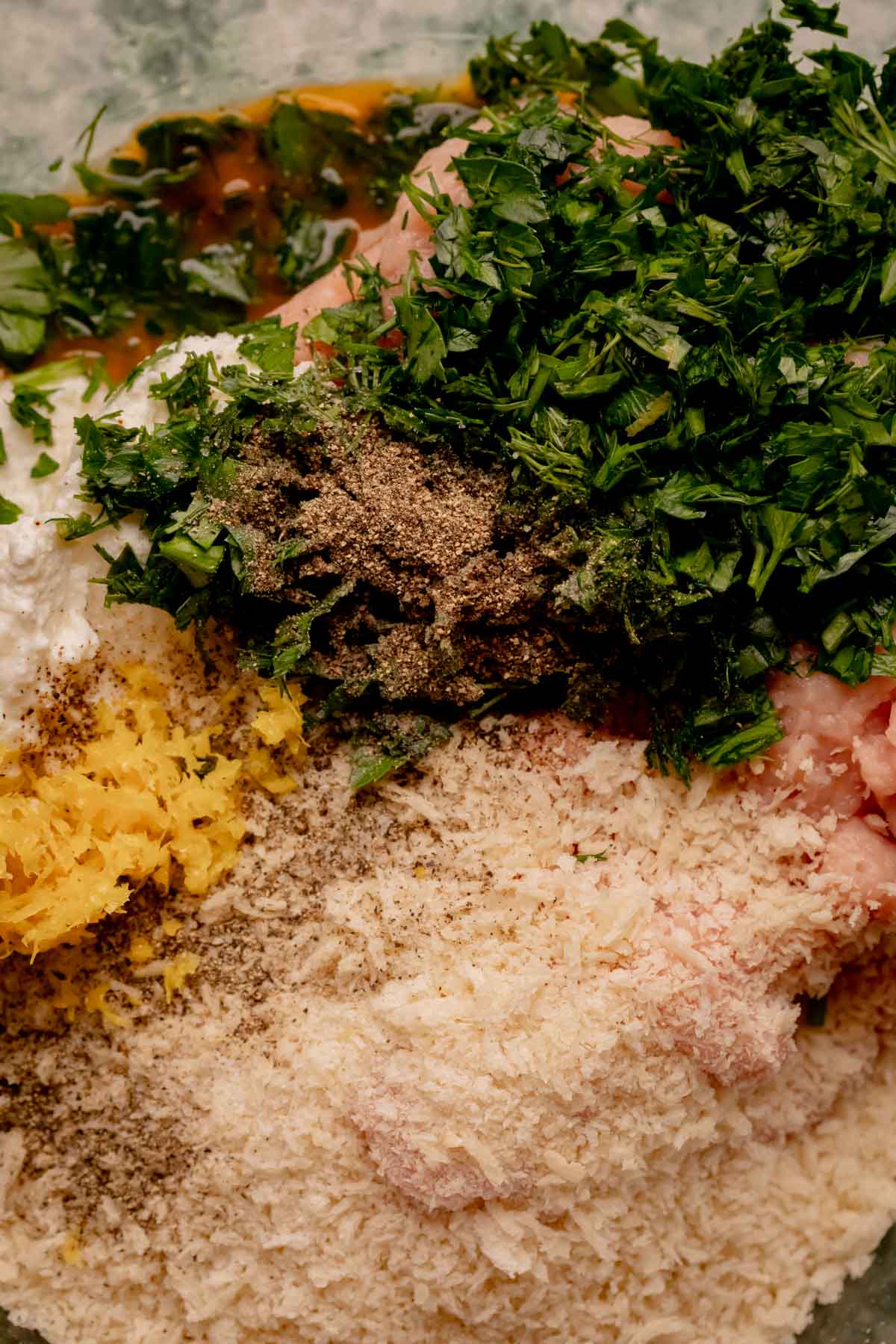 Ground chicken with herbs, breadcrumbs, and other ingredients in a bowl.