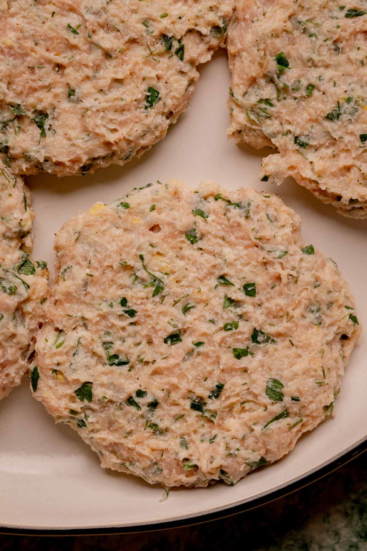 Raw herbed chicken patties on a plate.