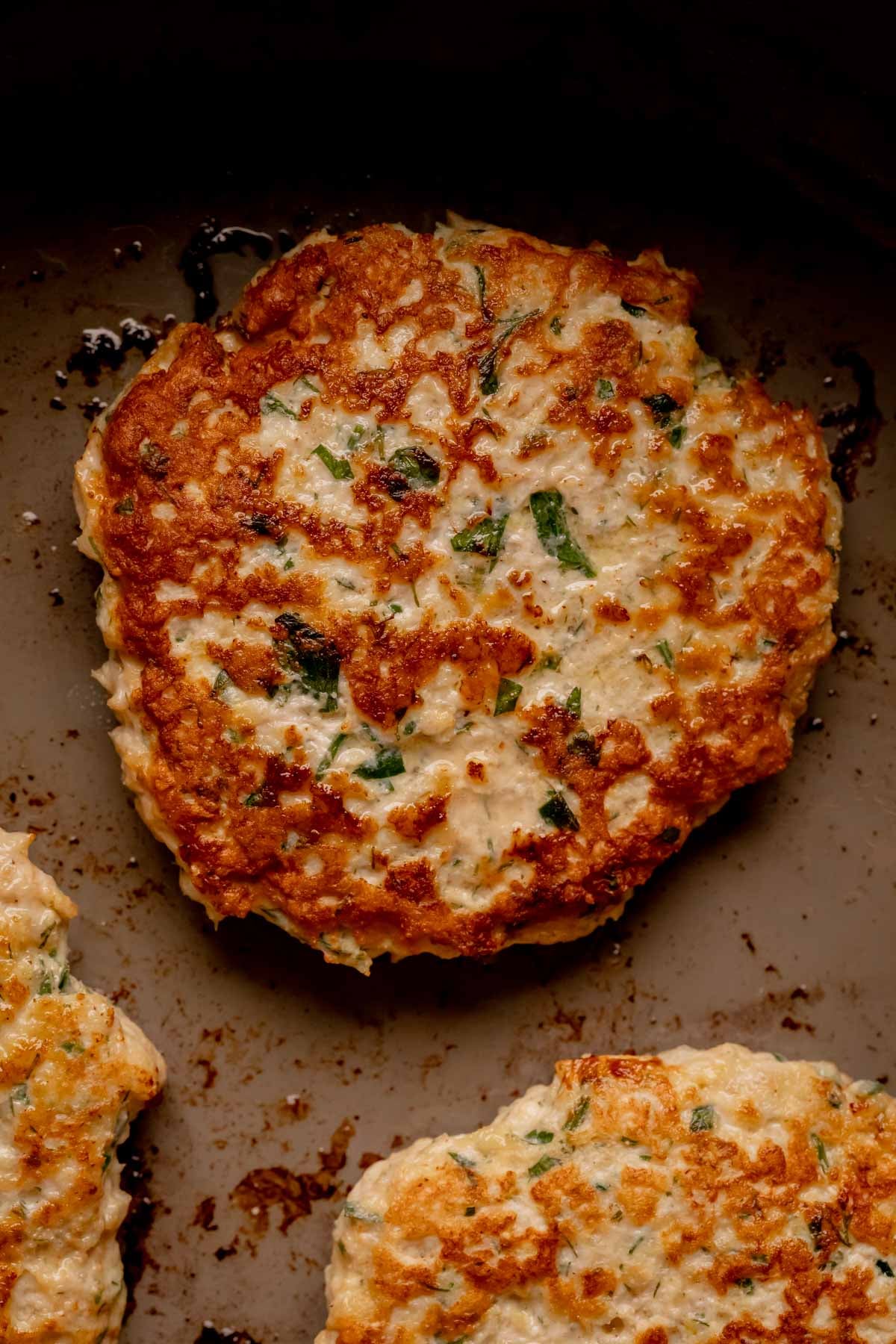 Cooked herbed chicken patties in a pan.