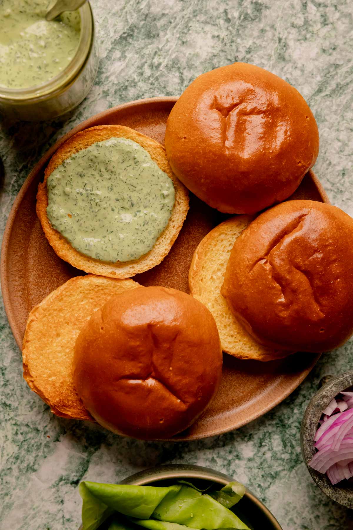 Brioche buns on a plate with butter lettuce, red onions, and green goddess sauce.