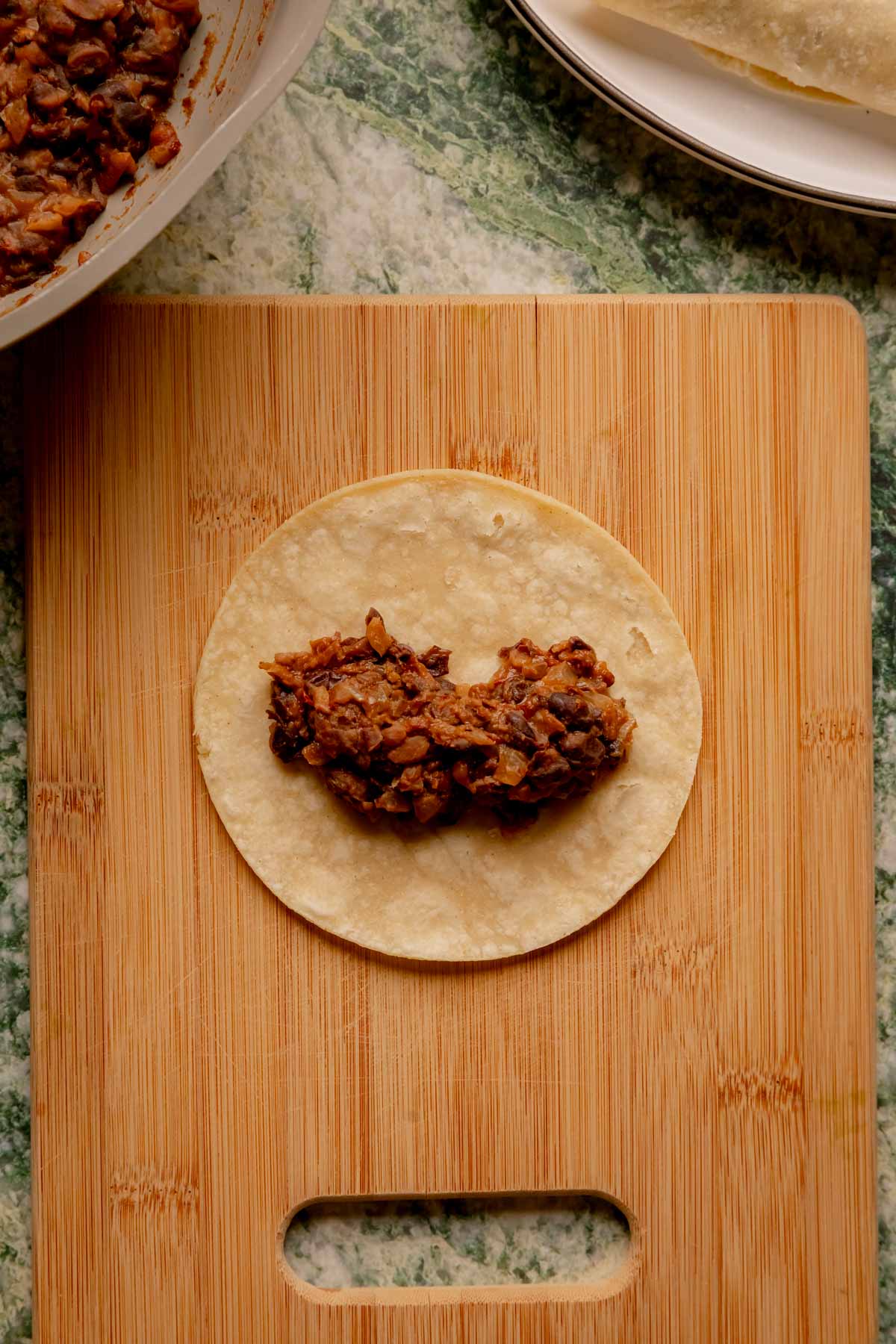 A tortilla being filled with black bean filling.