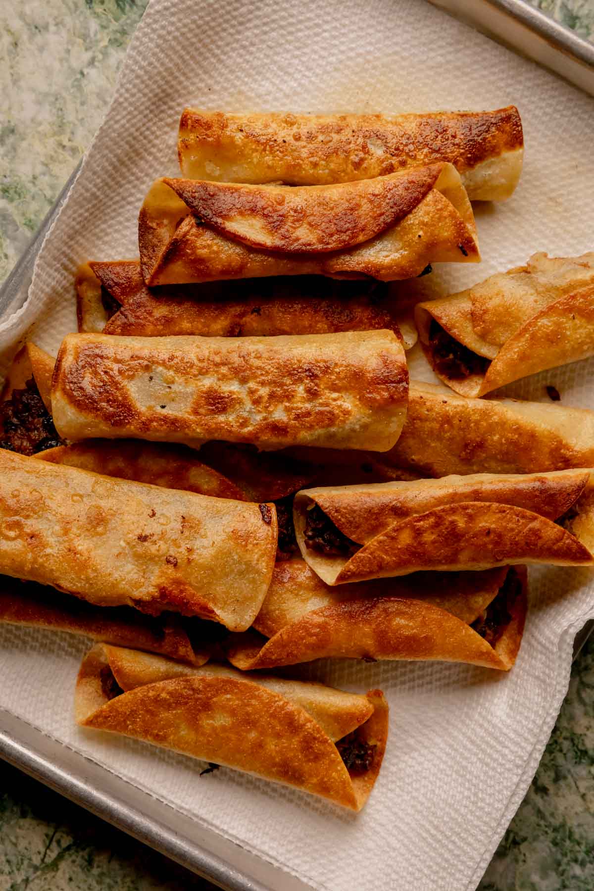 Cooked black bean flautas on a paper towel lined baking sheet.